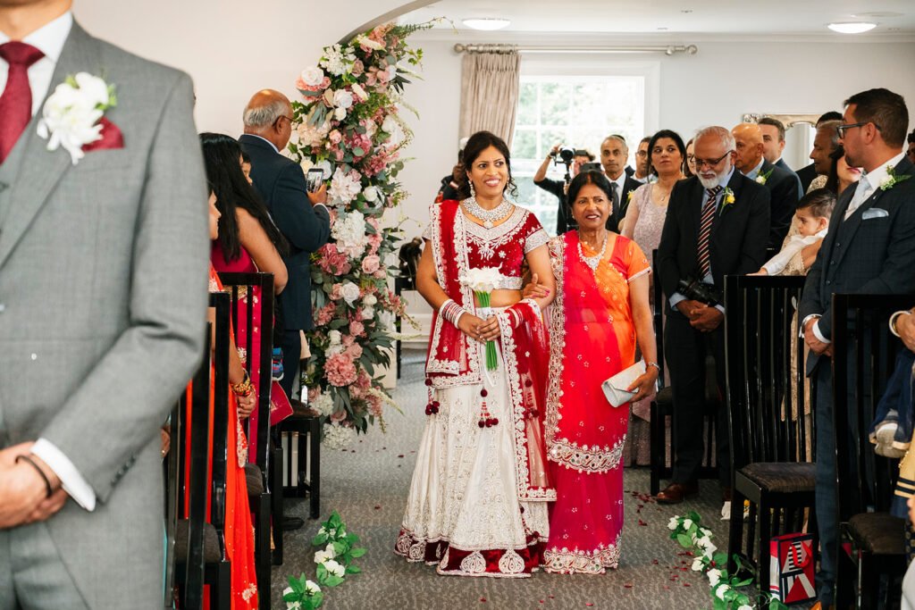 Indian bride in a traditional red and white lehenga walking down the aisle at Highfields House, Sandwell Register Office.